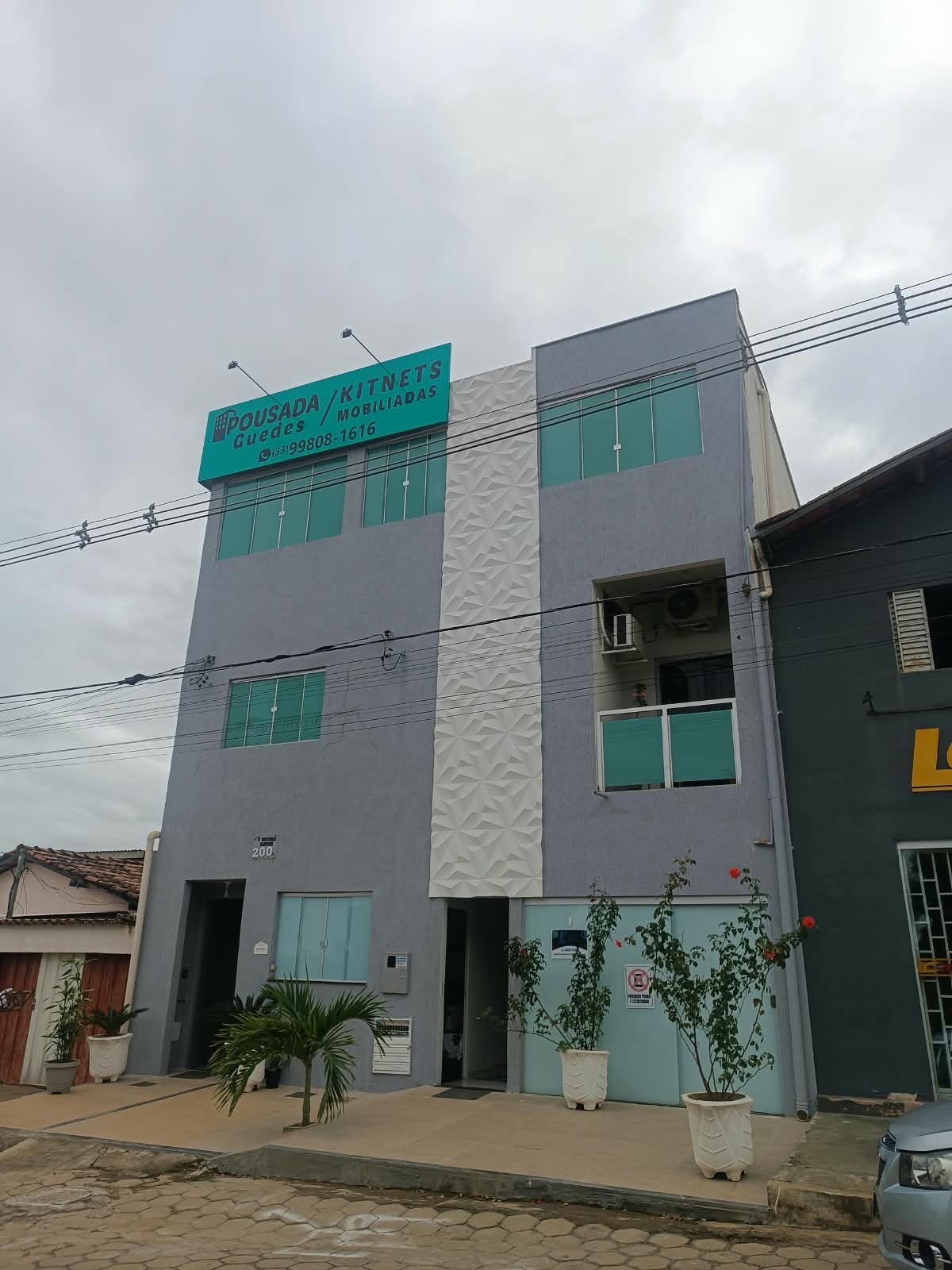 Fachada da Pousada Guedes, prédio cinza com placa verde-água Pousada Guedes / Kitnets Mobiliadas